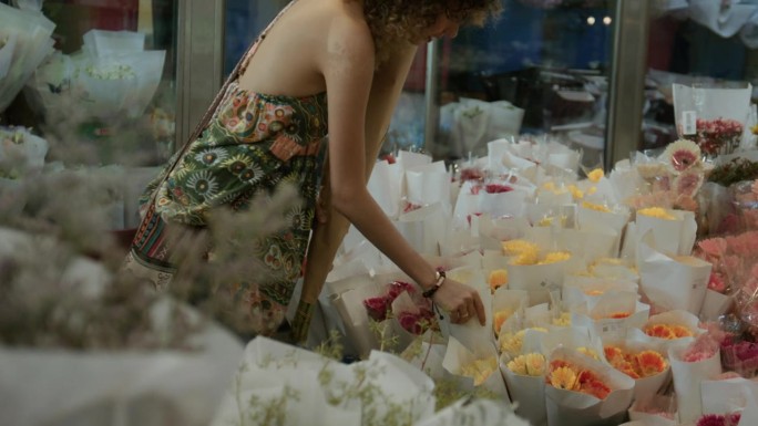 一位女顾客在花店选花。她最喜欢的花是五颜六色的非洲菊。