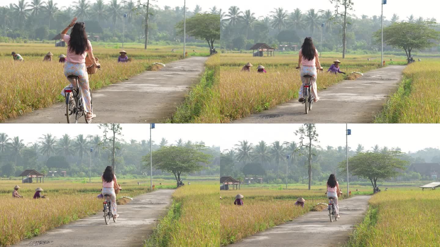 在村子里骑自行车，在农民收割水稻的背景下开心吗
