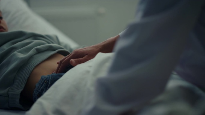 急诊病房里，医生触摸病人胃部特写。生病的孩子躺在床上