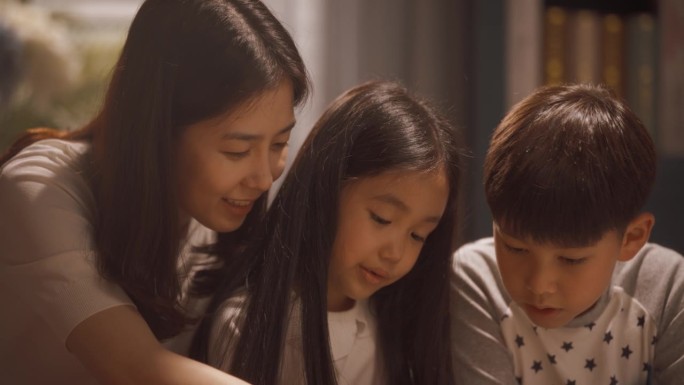 亚洲母亲带着可爱的儿子和女儿在家里使用平板电脑。年轻妈妈花时间与兄弟姐妹，培养孩子的教育，思维过程和