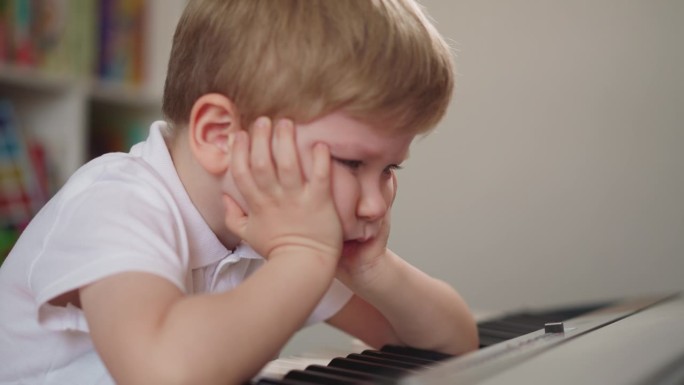 小男孩把胳膊肘放在钢琴键盘上，靠在手上