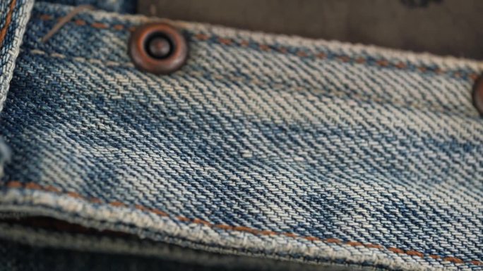 蓝色牛仔裤的旋转织物的特写细节。口袋上的铆钉和装饰补丁。