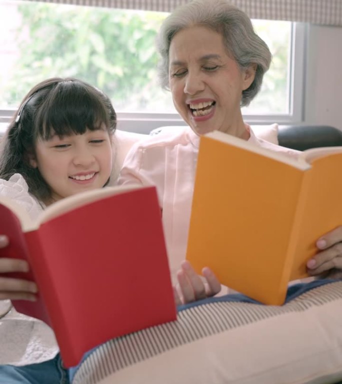 快乐的白发老妇和她的小孙女一起度过周末的活动，看封面是红色和橙色的书。靠近封面是红色和橙色的两本书。
