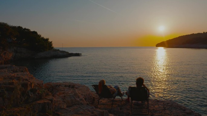 日落时分，一对夫妇在椅子上放松，看着平静的大海。就我们两个