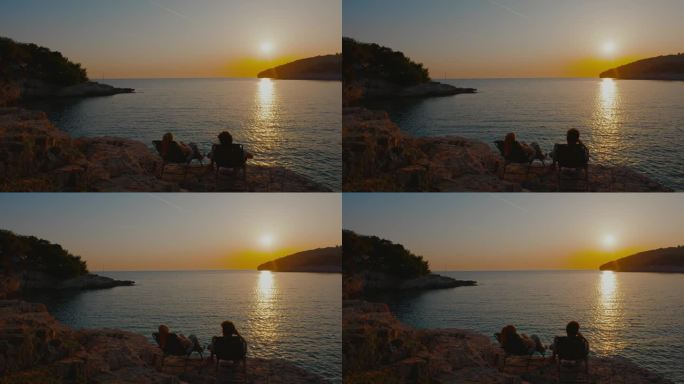 日落时分，一对夫妇在椅子上放松，看着平静的大海。就我们两个