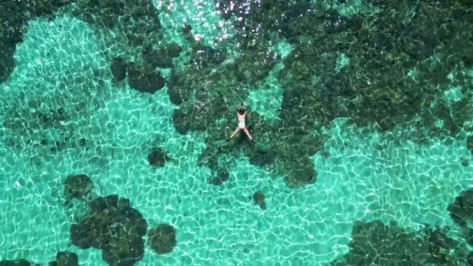 女性在海洋珊瑚礁周围浮潜的鸟瞰图