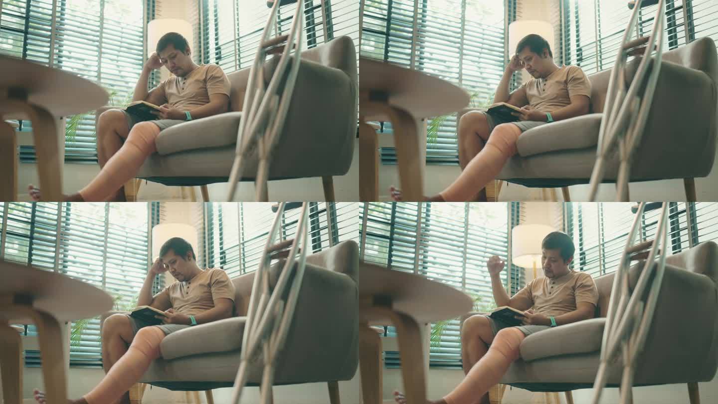 亚洲英俊的残疾男子坐在家里客厅的沙发上看书的肖像。