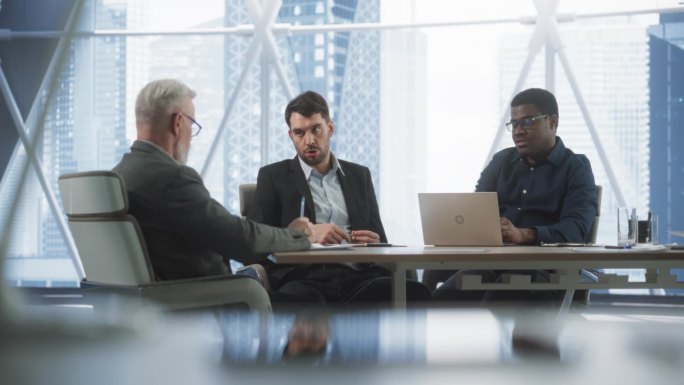 公司办公室会议室会议:三位不同的男性商业伙伴交谈，讨论投资机会，使用笔记本电脑。黑人和白人企业家经营