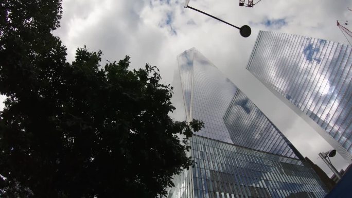 美国纽约曼哈顿，世界贸易中心纪念广场一号楼的低视角延时拍摄，多云的天空映照在玻璃摩天大楼上