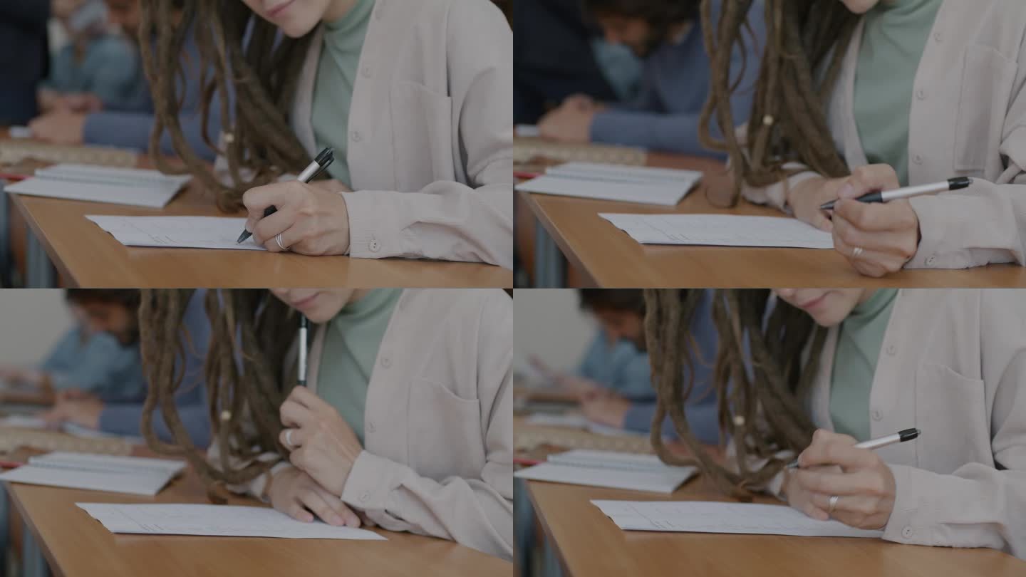 女学生和一群人坐在桌前写字，手拿笔通过考试的特写