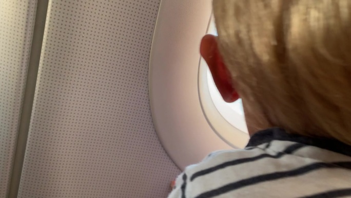 一个小男孩坐在飞机靠窗的地方，看着飞机上升