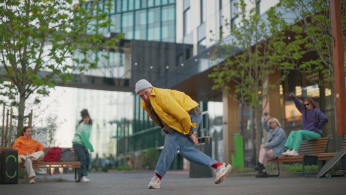 年轻时尚的B-boy在城市街道上的现代建筑之间跳霹雳舞。一群时尚的朋友在后台冷不防，支持霹雳舞演员练