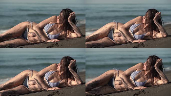 身穿比基尼的中年成年妇女躺在太平洋沙滩上晒日光浴，眼睛望向别处