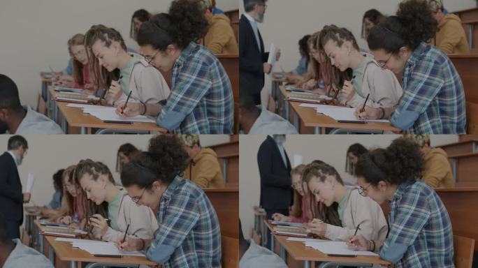 一群年轻人坐在课桌前写考试，老师在教室里走着