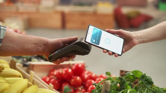 数字银行概念:消费者在农贸市场使用带有非接触式支付技术的手机支付天然商品。手持电子在线支付设备的街头