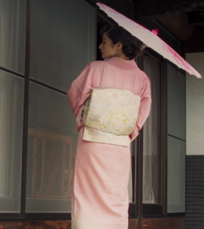 竖屏:日本女性看着镜头，温柔地微笑着，穿着传统的粉红色和服，带着花的装饰品，拿着伞。年轻美丽的女人在