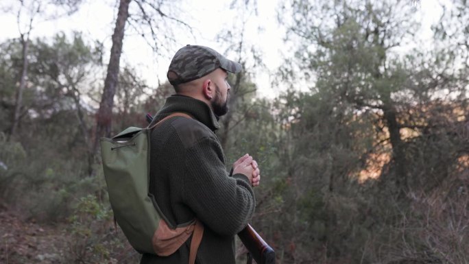 一个猎人拿着猎枪站在森林里四处张望。