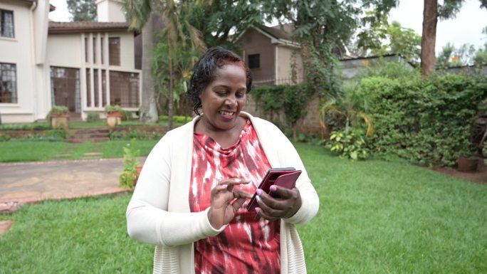 东非高级妇女在自家花园里发短信