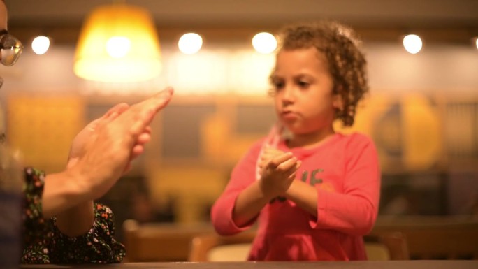 一位妇女教女儿在手上擦酒精凝胶/润肤霜/乳液。
