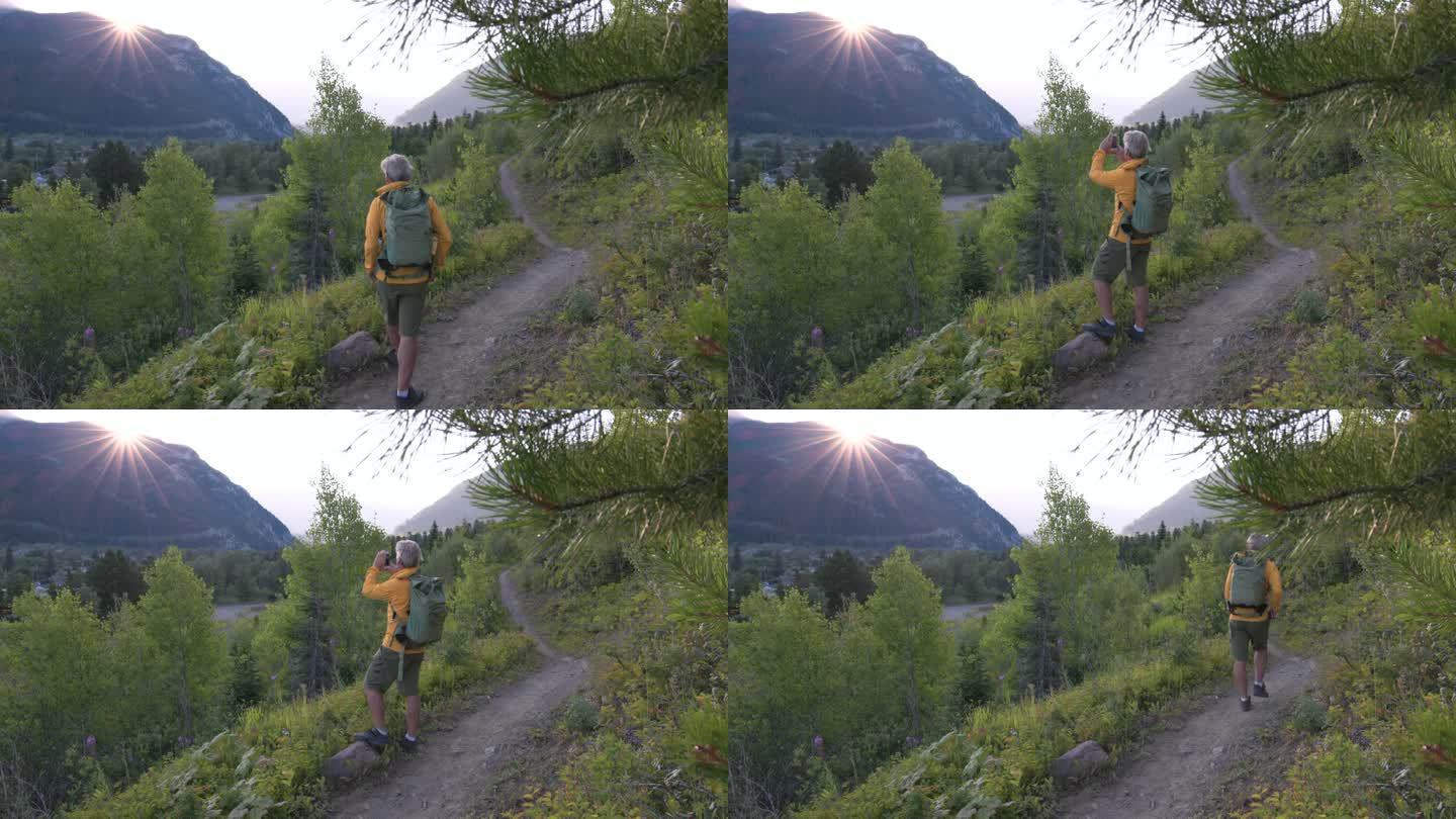 老人在日出时沿着山道徒步，拍照