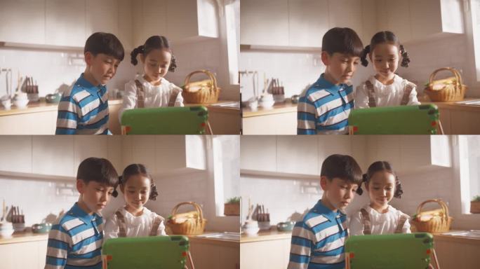 两个韩国孩子周末在厨房里使用电子平板电脑的照片。两个可爱的亚洲兄弟姐妹在线观看教育内容，分享小工具，