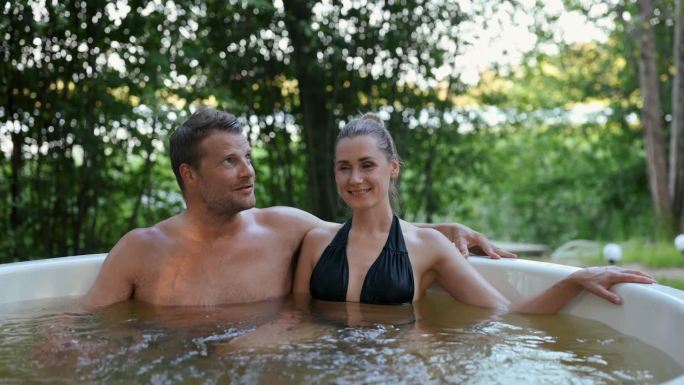一对浪漫的情侣在森林里的柴火户外热水浴缸里放松