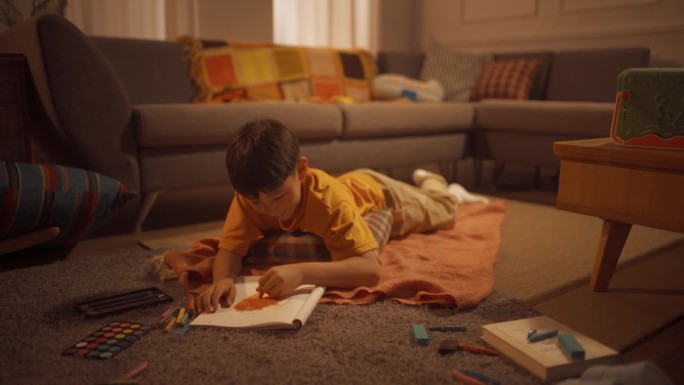 可爱的韩国男孩躺在地板上，用钢笔，铅笔，水彩画在笔记本上，在舒适的公寓里，温暖的光线。未来的艺术家是