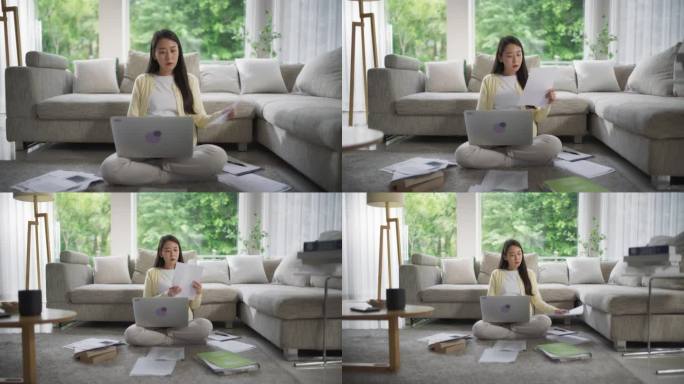 一位韩国妇女坐在地板上，在时尚明亮的客厅里用笔记本电脑做她的项目，与远程制作人团队合作创作一个创意写