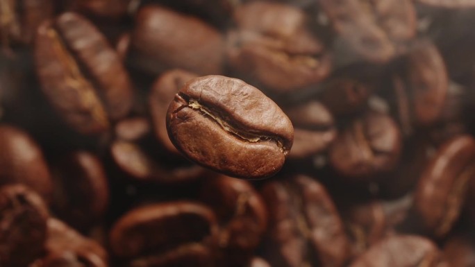 微距慢动作视频一个旋转的咖啡豆与焦外背景的烘焙咖啡豆，咖啡颗粒被笼罩在烟雾从烘焙。