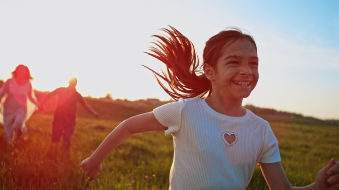 小女孩在草地上微笑着奔跑，她的父母跟在她后面跑
