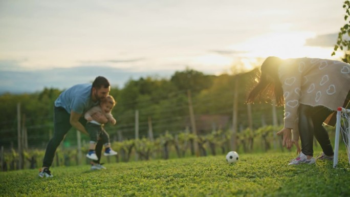 慢镜头:一对父母带着小男孩在绿地上踢足球