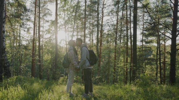 美丽的年轻夫妇在阳光普照的森林里手牵着手亲吻，享受大自然的慢动作