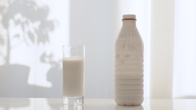 用塑料奶瓶滑动一杯牛奶。在白色天鹅绒窗帘的背景下