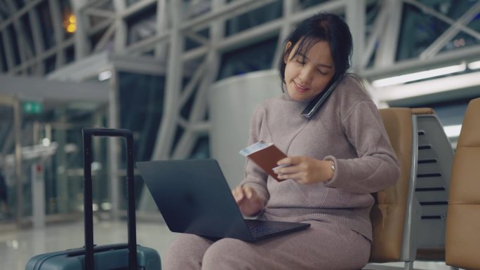 紫衣女子坐在机场候机区，打开笔记本电脑，用手机和朋友谈论旅行