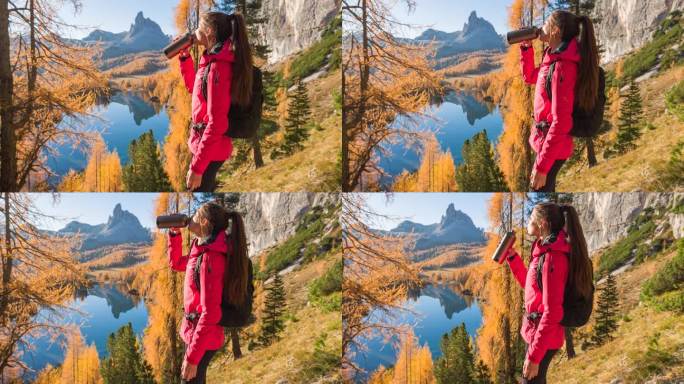女人在山腰喝水，同时俯瞰雄伟的山间湖泊在秋天