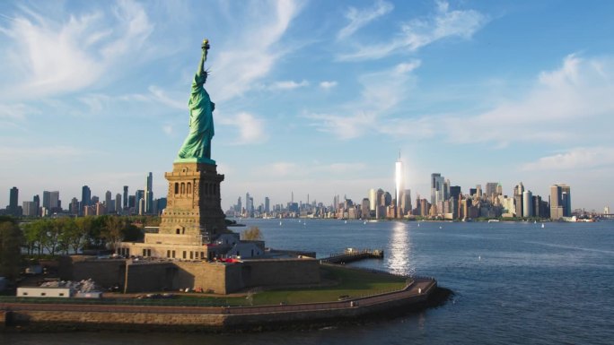 空中直升机的电影通过视图的自由女神像与曼哈顿天际线城市景观。在一个阳光明媚的日子里，纽约市摩天大楼和