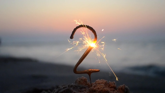 孟加拉火火花在数字2的形状燃烧和闪闪发光在沙滩上的海岸在日落的黎明。概念假期生日新年聚会庆祝