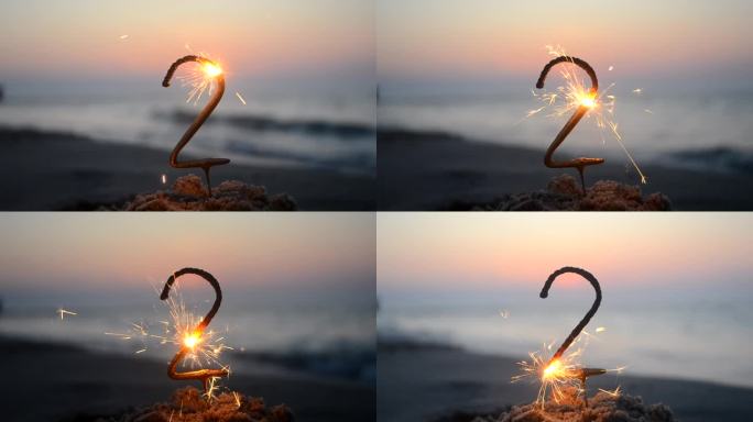 孟加拉火火花在数字2的形状燃烧和闪闪发光在沙滩上的海岸在日落的黎明。概念假期生日新年聚会庆祝