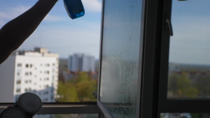 不认识的人在玻璃上喷洒窗户清洁剂，安装窗户清洁机器人工作的侧视图。家务助理，保持清洁