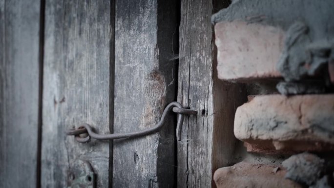 老旧的木门，锁在一个钢钩上，特写。暗淡，不饱和的颜色和相机抖动