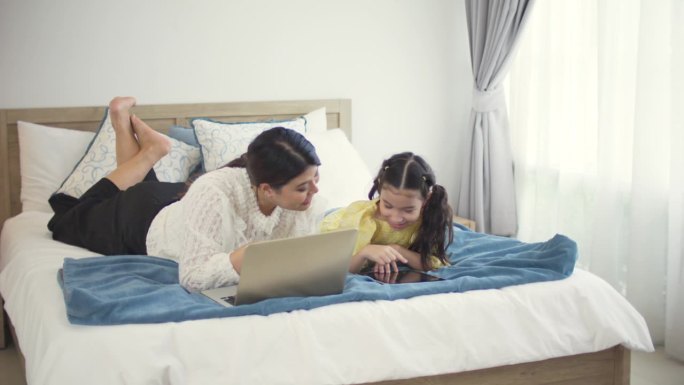 母亲和女儿在卧室使用笔记本电脑和平板电脑，单身妈妈