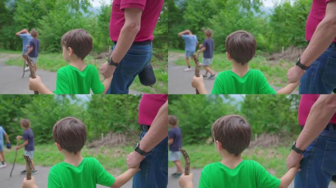 家庭周末活动的场景，孙子和爷爷手牵着手在大自然中远足。4岁的小男孩和他的爷爷在小路上