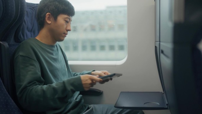 亚洲人在白天乘火车旅行。一个人坐在窗边，打开笔记本，开始在键盘上打字。