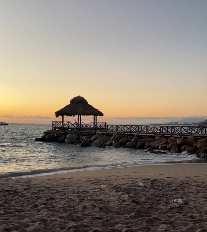 海滩上的亭子，海湾的石头和木头在日落时在海上与船只的背景