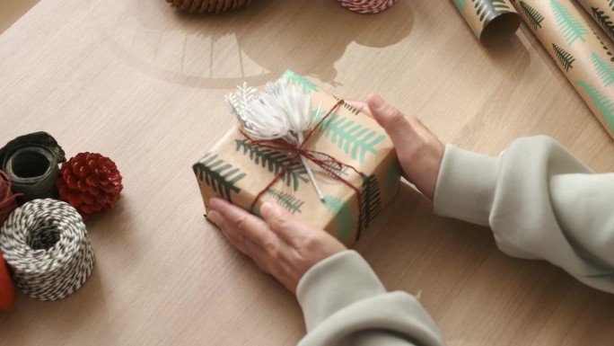 近距离用手工包装纸和鲜花装饰圣诞礼物，放在桌子上。为新年节日准备礼物。