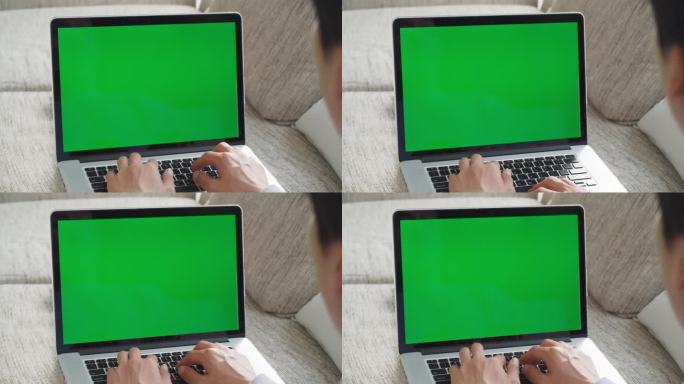 一名身份不明的男子沉浸在办公室工作中，在沙发上舒适的家庭工作空间中使用带有绿屏模拟显示的笔记本电脑进