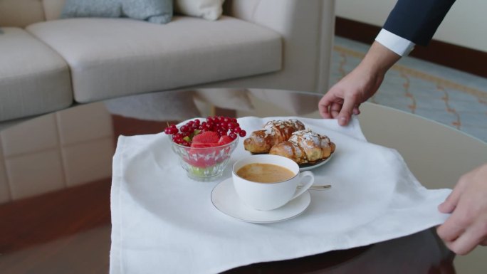 经理为客人提供早餐，桌上有咖啡、羊角面包和水果