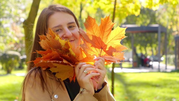 在秋天的公园里，快乐的微笑的女人捧着红枫树跳舞，笑着。美在自然，落在城市，幸福女人。