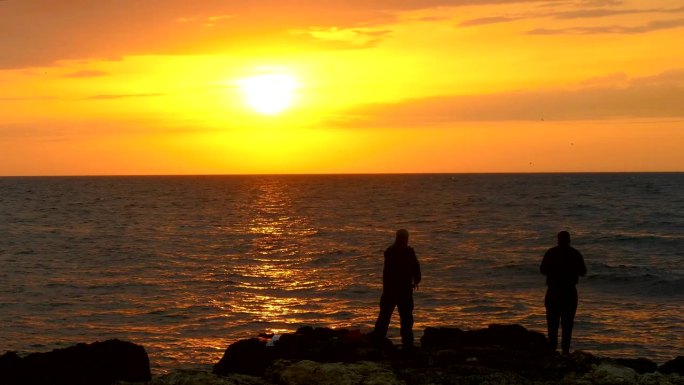 日落时在岸边钓鱼金色夕阳两个人站在海边天