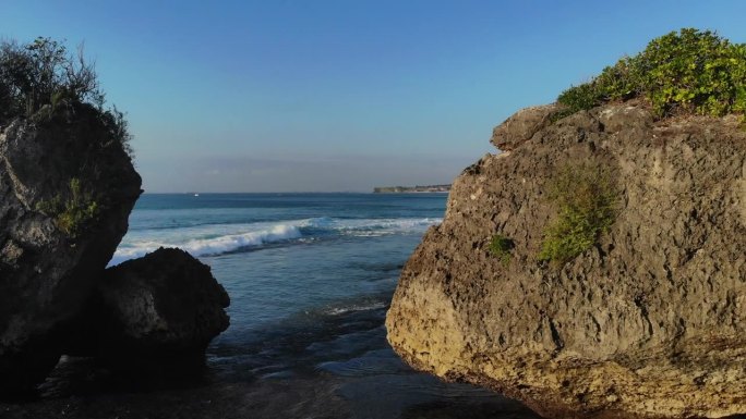 在一个阳光明媚的日子里，在海岸的两个大岩层之间飞行，被大自然包围。开阔的蓝色海洋和白色的波浪在背景中